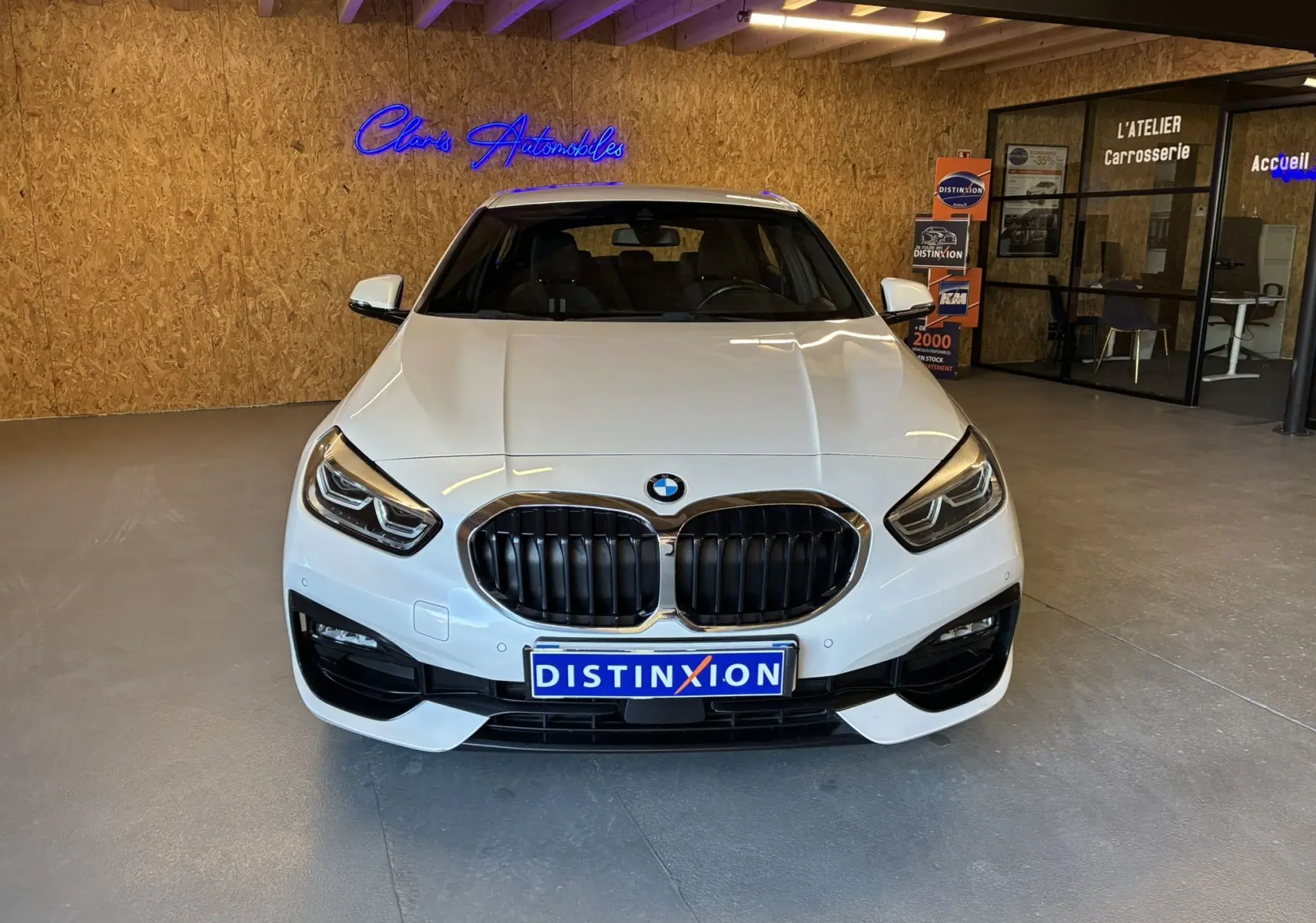 Vue frontale d'une BMW Série 1 118i Edition Sport blanche avec calandre noire et phares LED dans un showroom.
