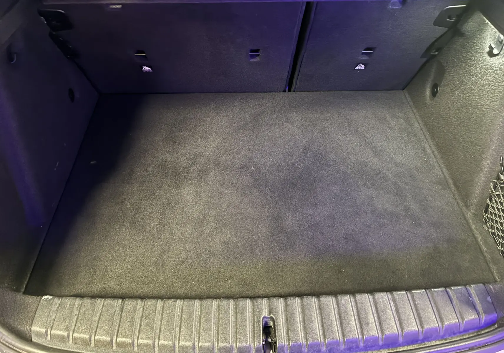 Coffre spacieux et propre de la BMW Série 1 118i Edition Sport 2023, vue intérieure depuis l'arrière, tapis noir.