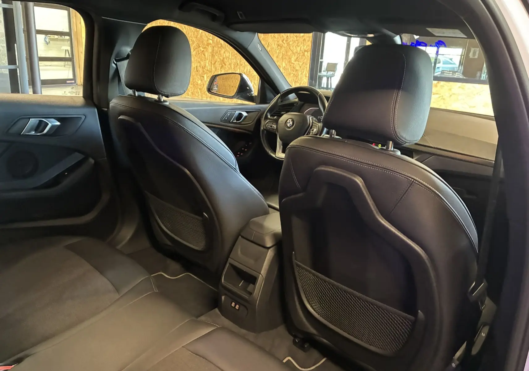 Vue intérieure arrière de la BMW Série 1 118i Edition Sport 2023 avec sièges noirs en tissu et cuir, volant visible côté gauche.