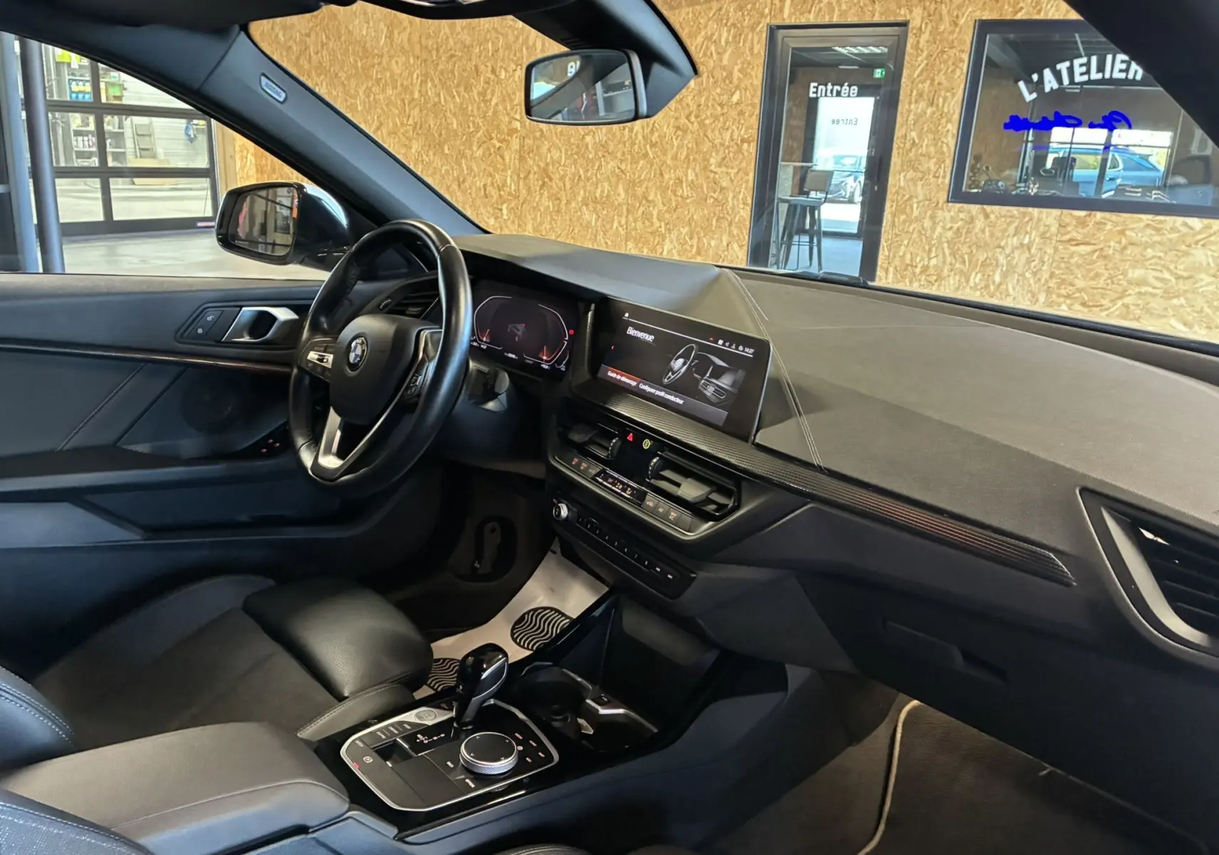 Vue intérieure côté conducteur de la BMW Série 1 118i Edition Sport 2023 avec tableau de bord noir et écran tactile.