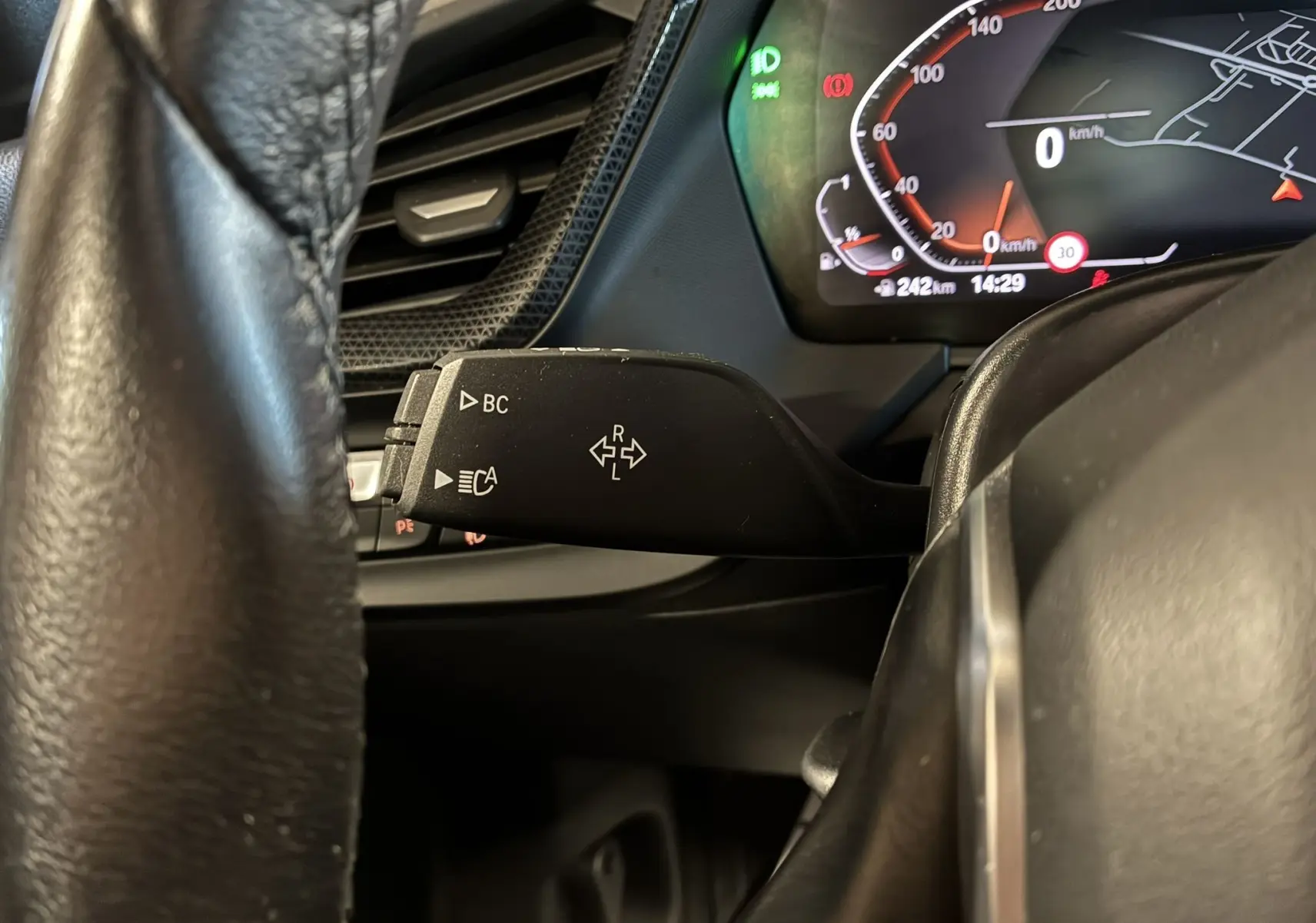 Gros plan sur la commande de clignotant à gauche du volant d'une BMW Série 1 blanche, tableau de bord numérique visible.