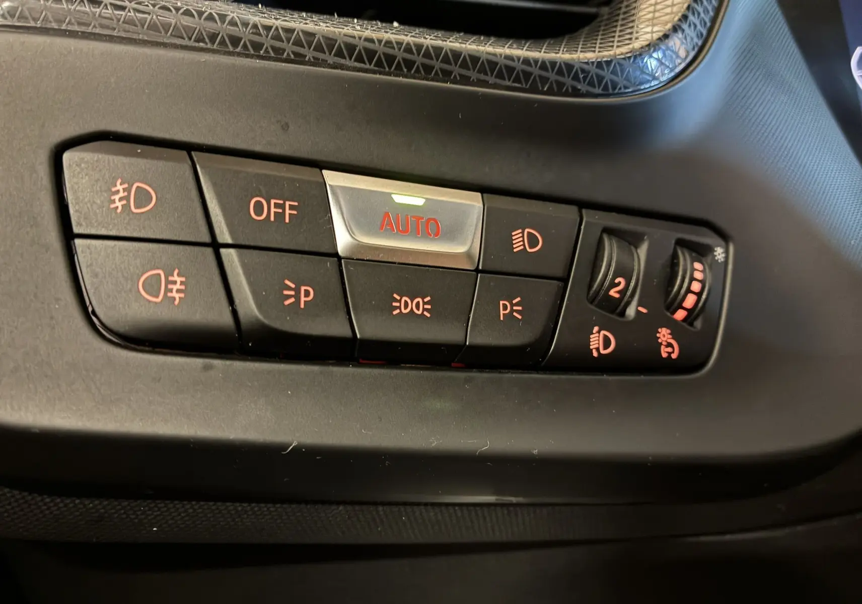 Gros plan sur les commandes d'éclairage avec bouton AUTO illuminé dans l'habitacle noir d'une BMW Série 1 blanche 118i Edition Sport.