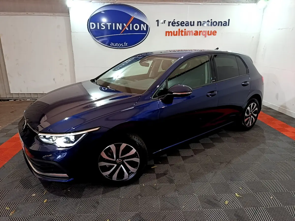 Volkswagen Golf 1.0 TSI bleu en 3/4 avant droit avec phares allumés dans un showroom intérieur.