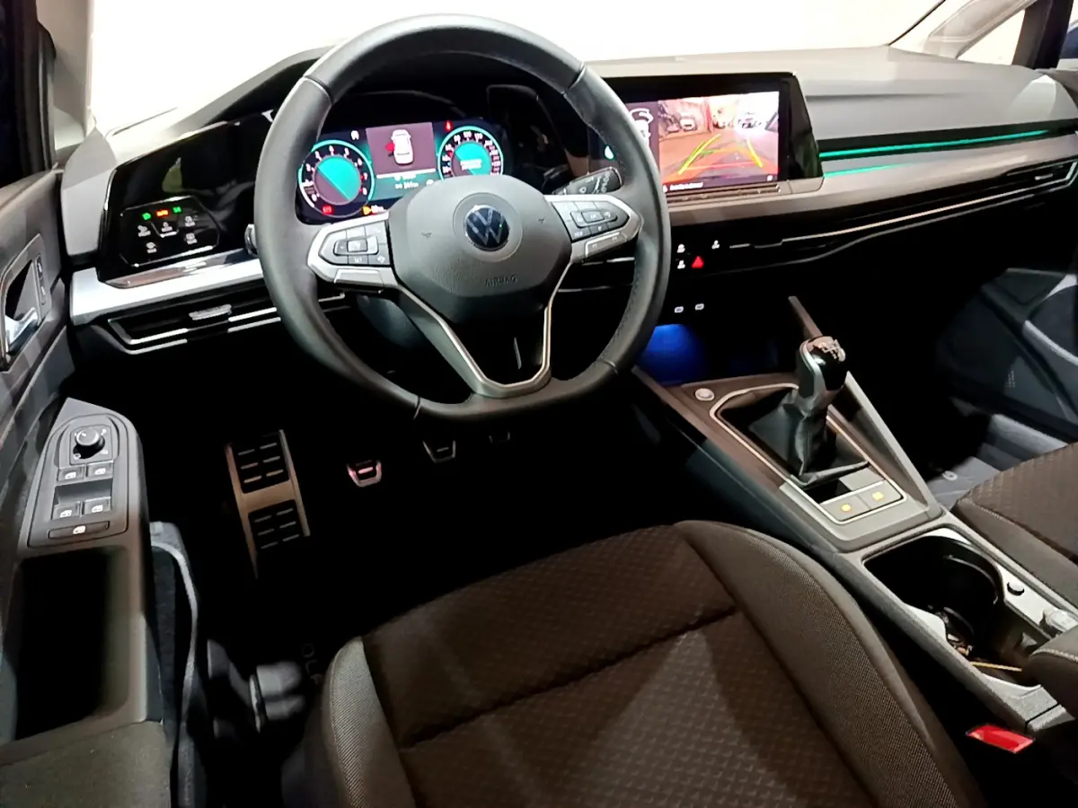Vue intérieure avant de la Volkswagen Golf 1.0 TSI avec volant cuir, écran tactile et levier de vitesse manuel.