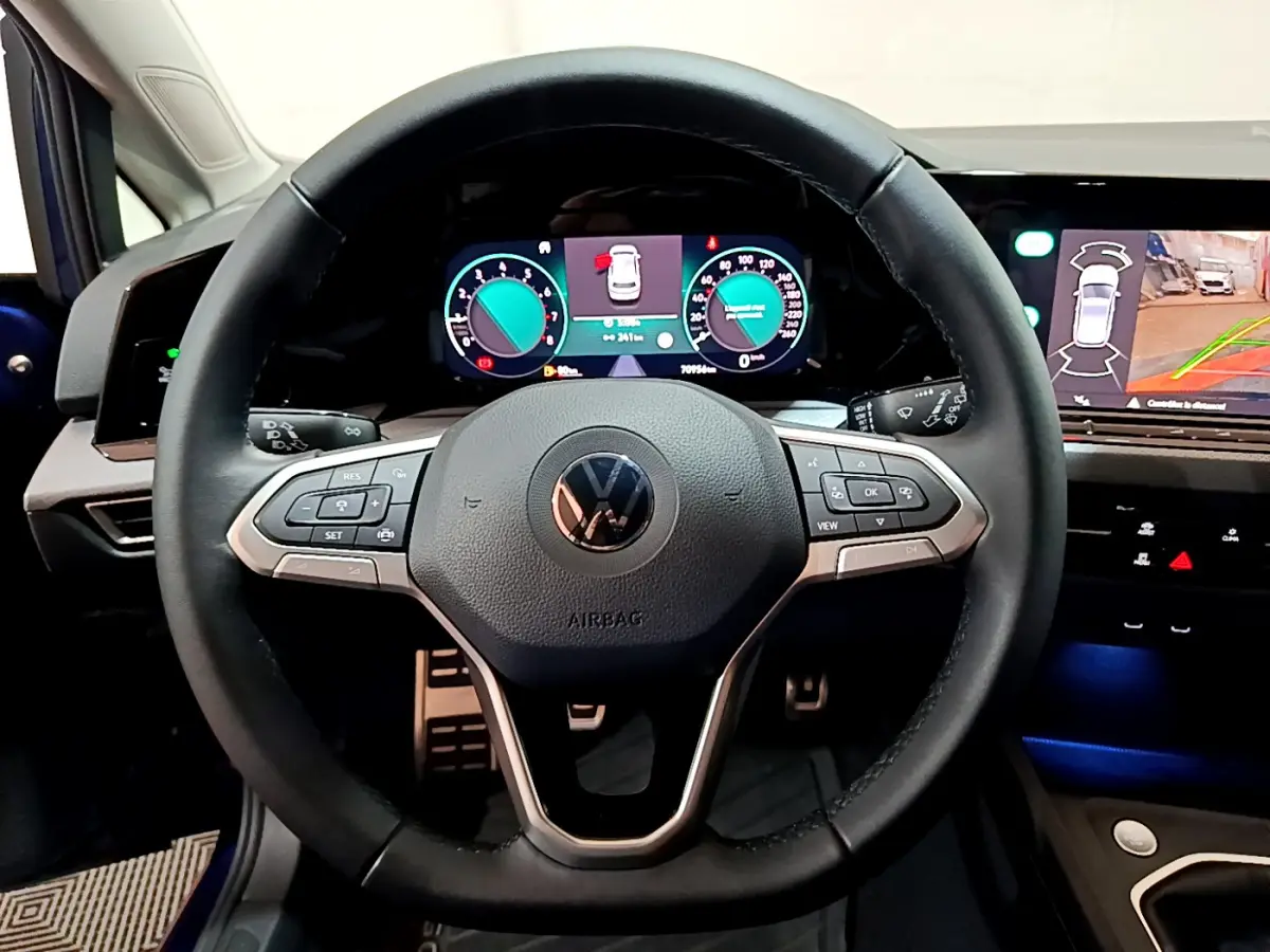 Vue centrée sur le volant cuir multifonctions et les écrans digitaux du tableau de bord de la Volkswagen Golf bleue 2022.