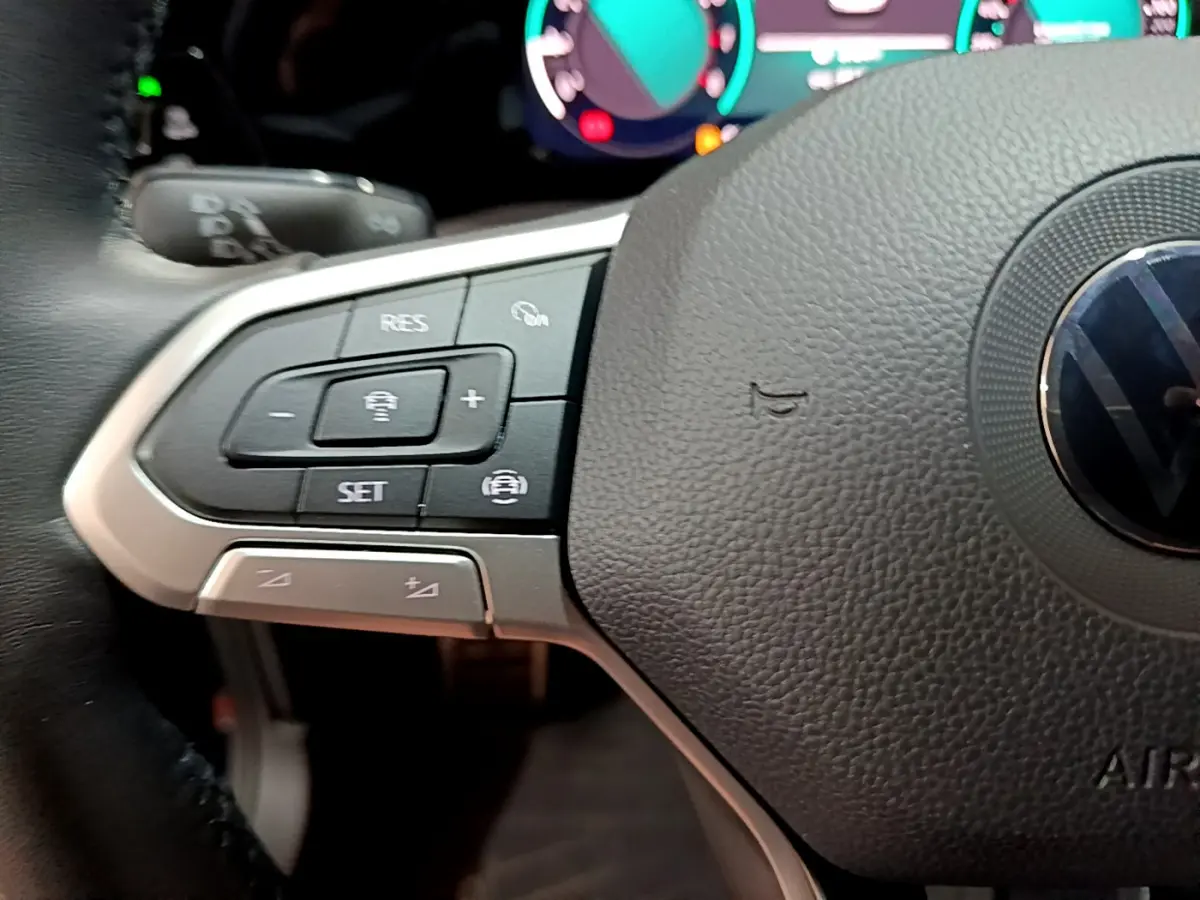 Gros plan sur le volant cuir multifonctions de la Volkswagen Golf 1.0 TSI bleu, avec commandes de régulateur de vitesse visibles.