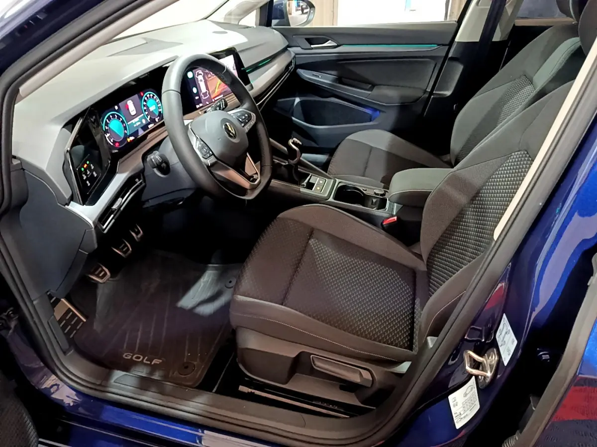 Vue intérieure côté conducteur d'une Volkswagen Golf bleue 2022 avec tableau de bord numérique et sièges tissu noirs.