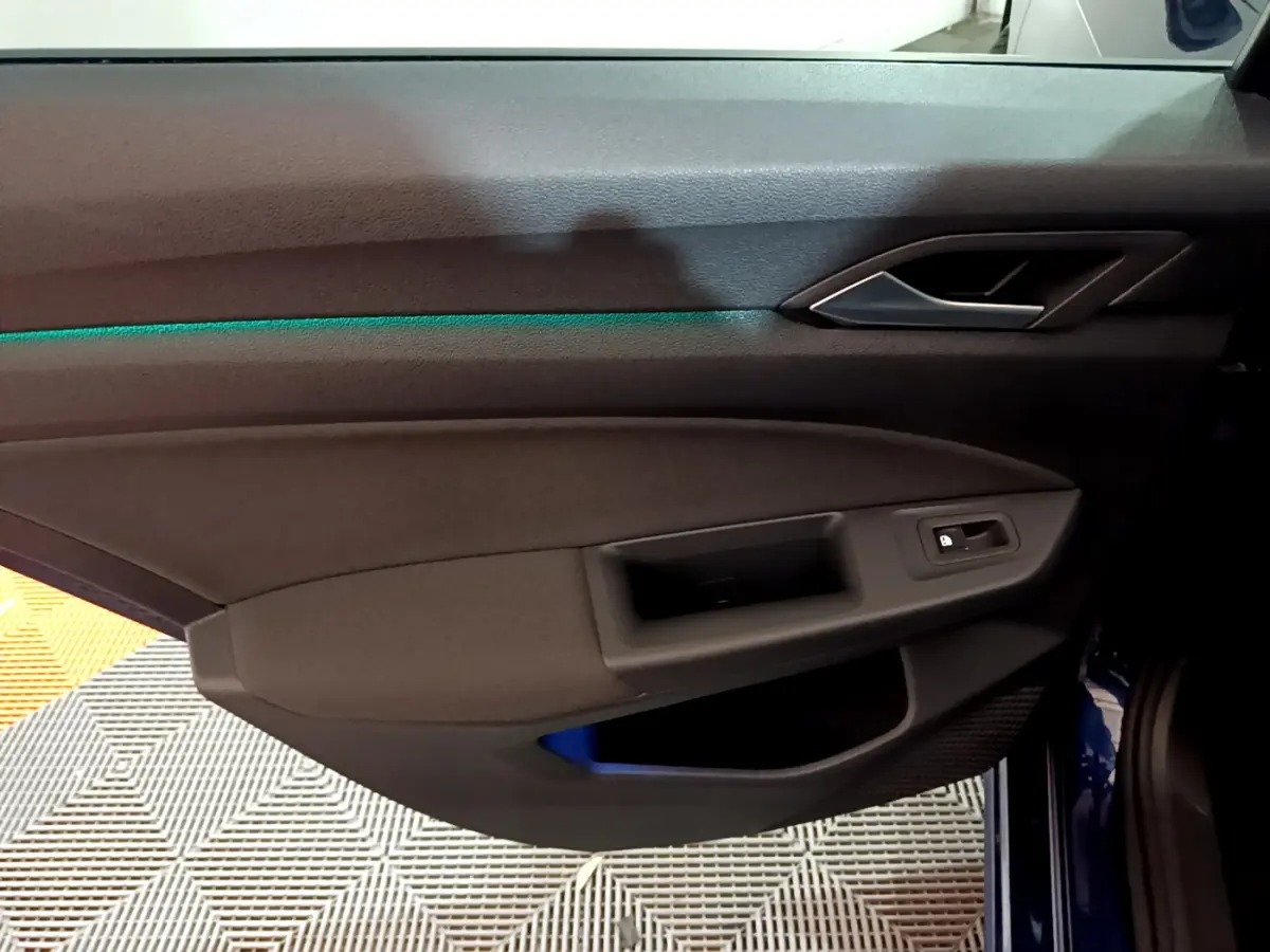 Vue rapprochée de la porte côté gauche de la Volkswagen Golf bleue 2022, avec éclairage d'ambiance vert subtil.