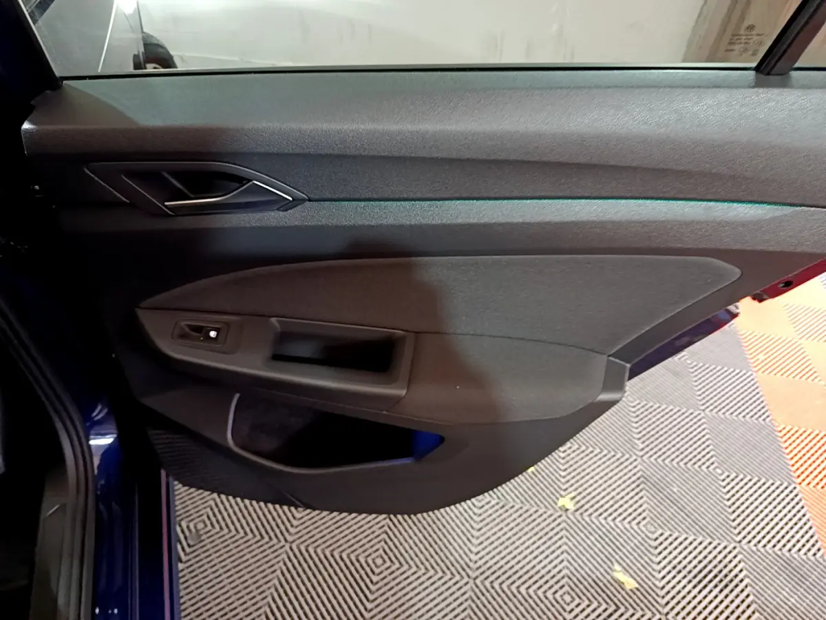 Porte côté gauche ouverte d'une Volkswagen Golf 1.0 TSI bleu 2022, avec poignée intérieure et commande de lève-vitre.