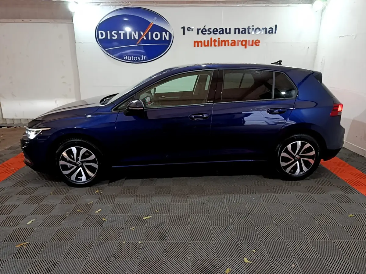 Profil latéral droit d'une Volkswagen Golf 1.0 TSI bleu foncé dans un showroom avec logo Distinxion en arrière-plan.