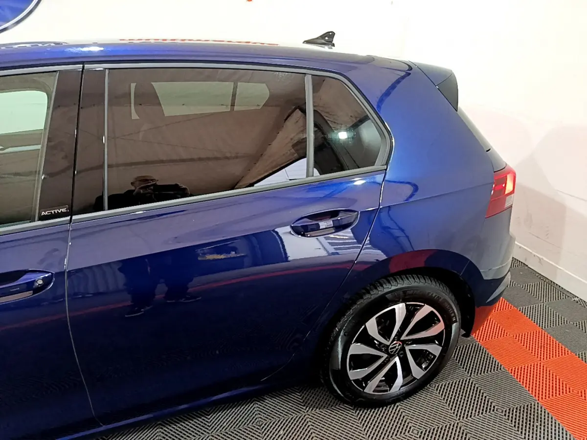 Vue côté gauche arrière d'une Volkswagen Golf 1.0 TSI Active bleu avec jante alliage et vitres teintées.