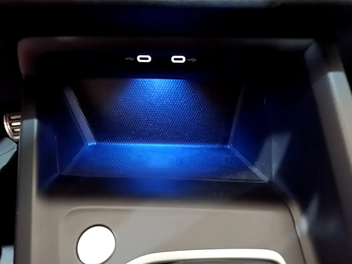 Gros plan sur la zone de recharge à induction éclairée en bleu dans le compartiment central d'une Volkswagen Golf bleue 2022.