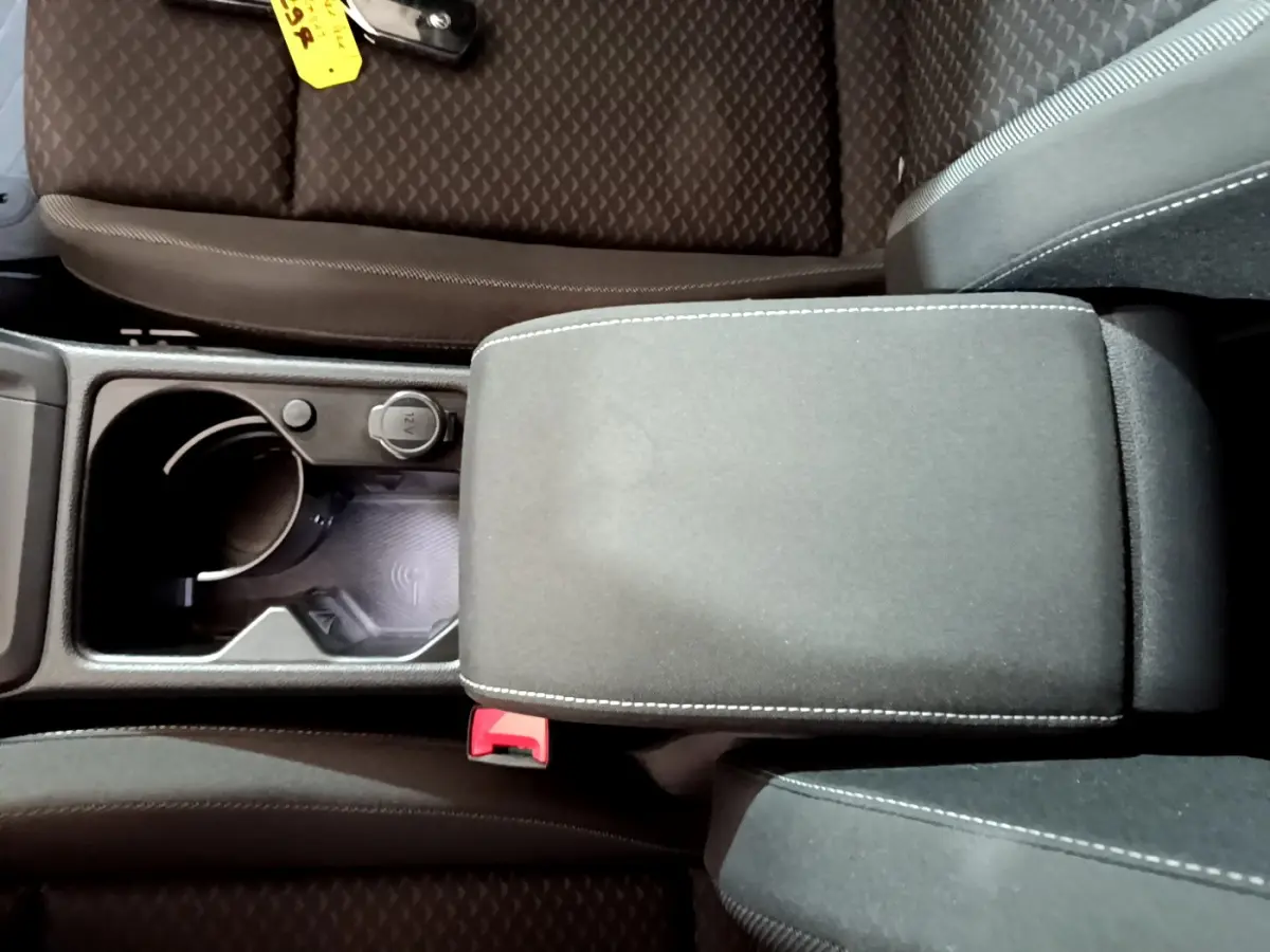 Vue plongeante sur la console centrale noire de la Volkswagen Golf 1.0 TSI avec accoudoir et prise 12V visible.