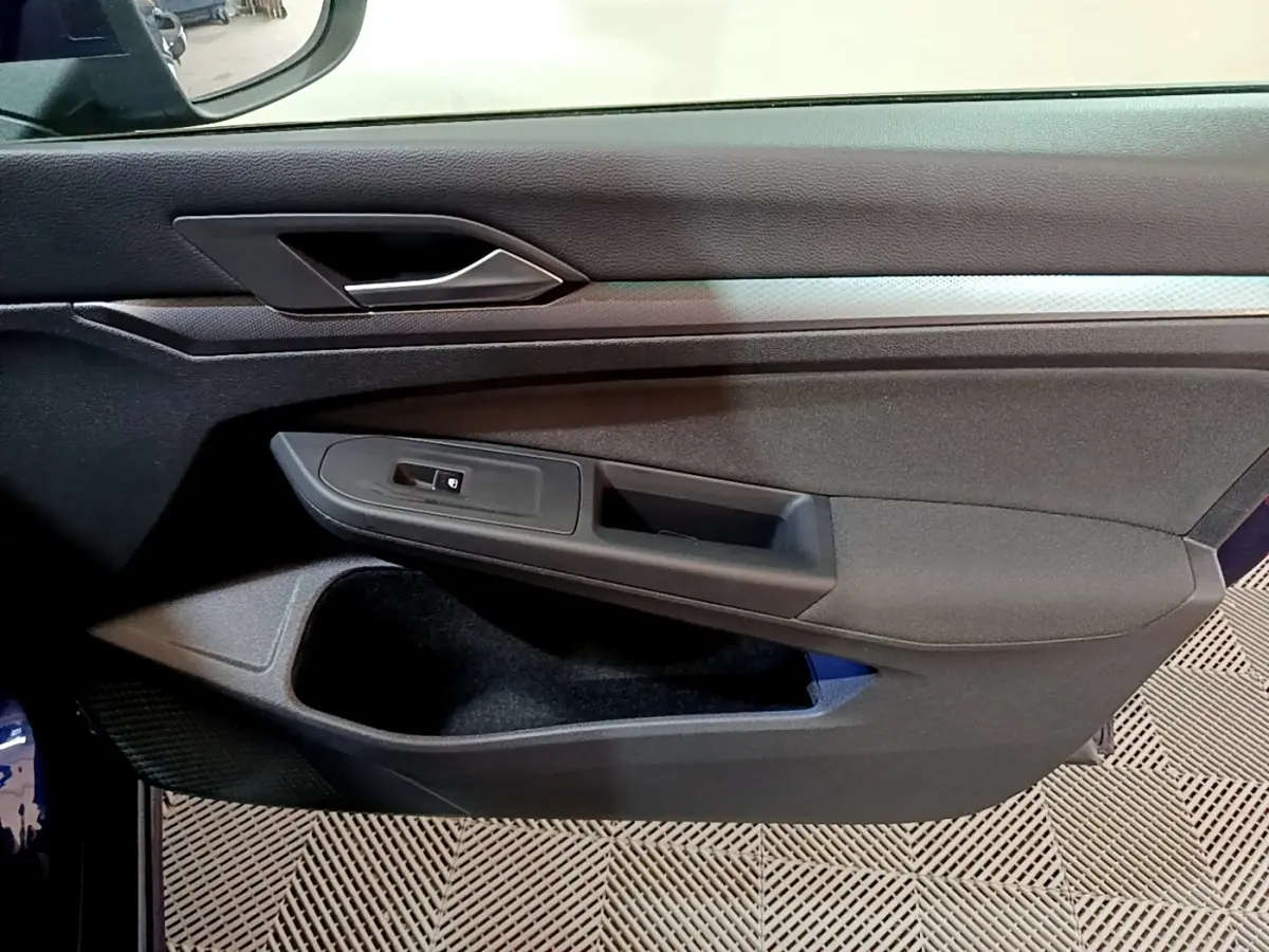 Vue rapprochée de la porte côté gauche d'une Volkswagen Golf bleu 2022 avec poignée argentée et commandes de vitre noires.
