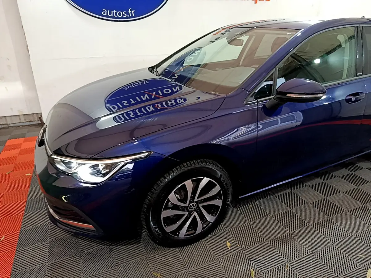 Vue 3/4 avant droit d'une Volkswagen Golf bleu métallisé avec phares LED allumés et jantes alliage distinctives.