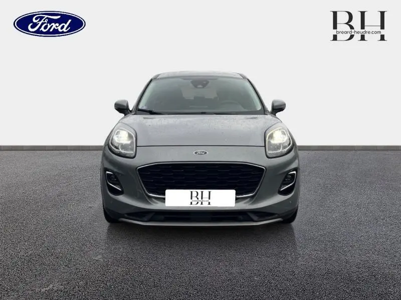 Vue de face d'une Ford Puma 2023 gris Solar métallisé avec calandre noire et phares allumés sur fond neutre.