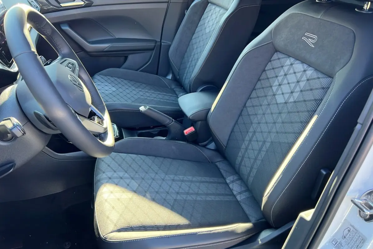 Vue intérieure côté conducteur du Volkswagen T-Cross blanc, sièges tissu R-Line avec surpiqûres et volant cuir multifonctions.