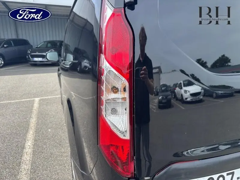 Gros plan sur le feu arrière droit du Ford Transit Connect L1 noir Agate Métallisée, avec reflet du parking en arrière-plan.