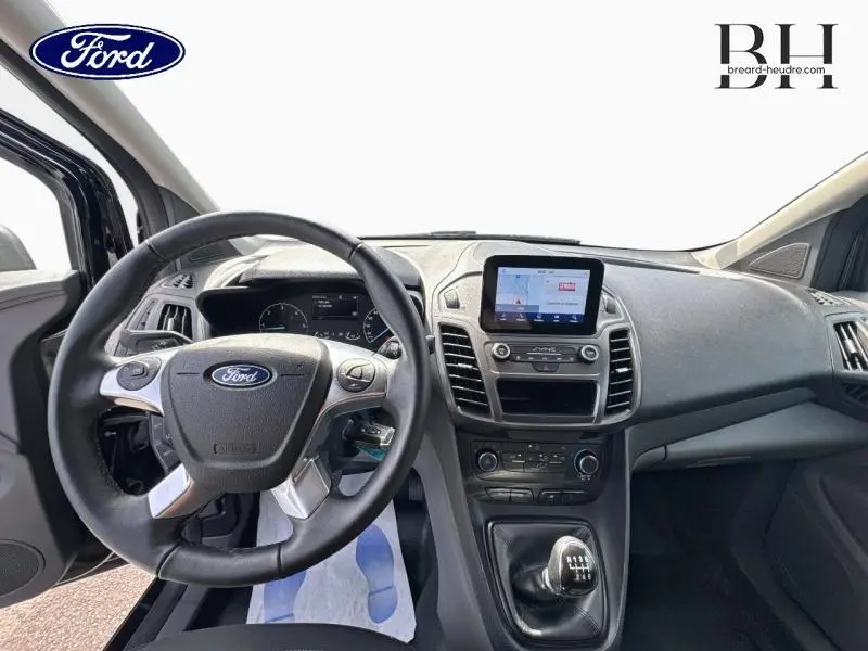Vue intérieure avant du Ford Transit Connect L1 2023, tableau de bord noir avec volant multifonction et écran tactile central.