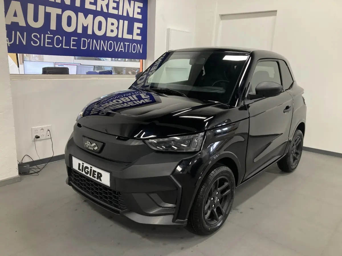 Vue 3/4 avant d'une Ligier JS50 noire 2026 avec jantes alu noires et feux LED en intérieur showroom.