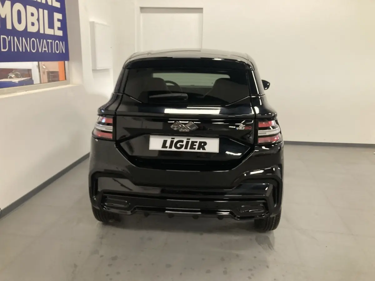 Vue arrière d'une Ligier JS50 0.5 REVO D+ Select noire, avec feux LED et jantes alu noires en intérieur showroom.
