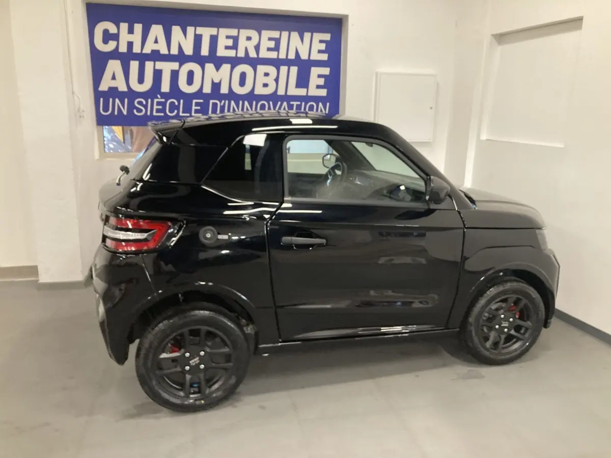 Vue de profil côté gauche d'une Ligier JS50 noire 2026 avec jantes alu noires et feux arrière LED en intérieur showroom.