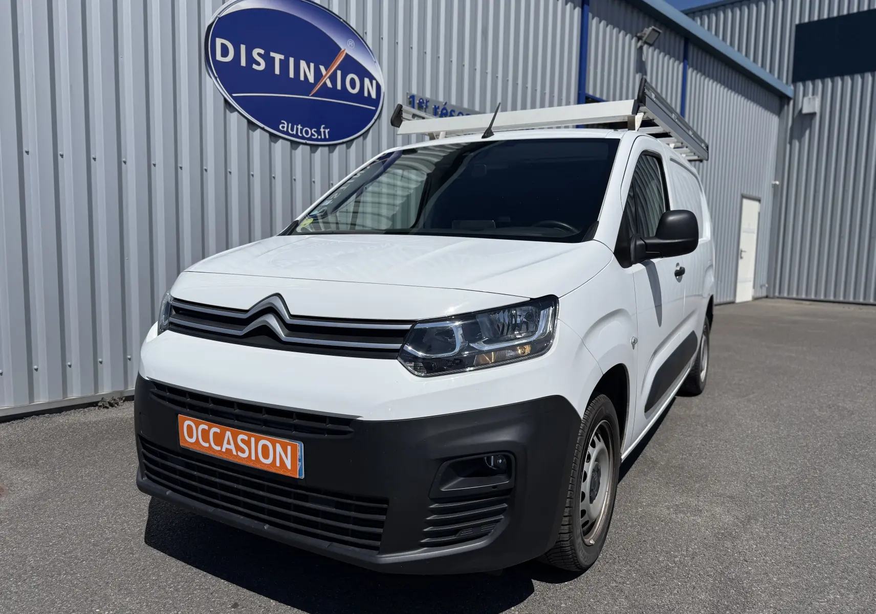 Citroën Berlingo XL blanc banquise en 3/4 avant droit avec galerie de toit et pare-chocs noirs visibles.