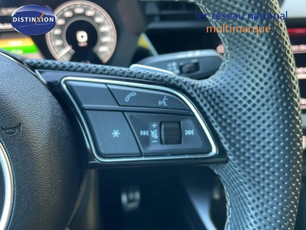 Gros plan sur les commandes gauche du volant en cuir perforé de l'Audi A3 Sportback noire 2025, affichage numérique en arrière-plan.