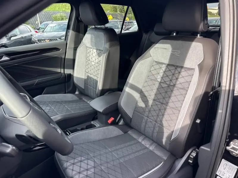 Vue intérieure côté conducteur du Volkswagen T-Roc 2025, sièges R-Line en tissu et cuir noir avec surpiqûres grises.