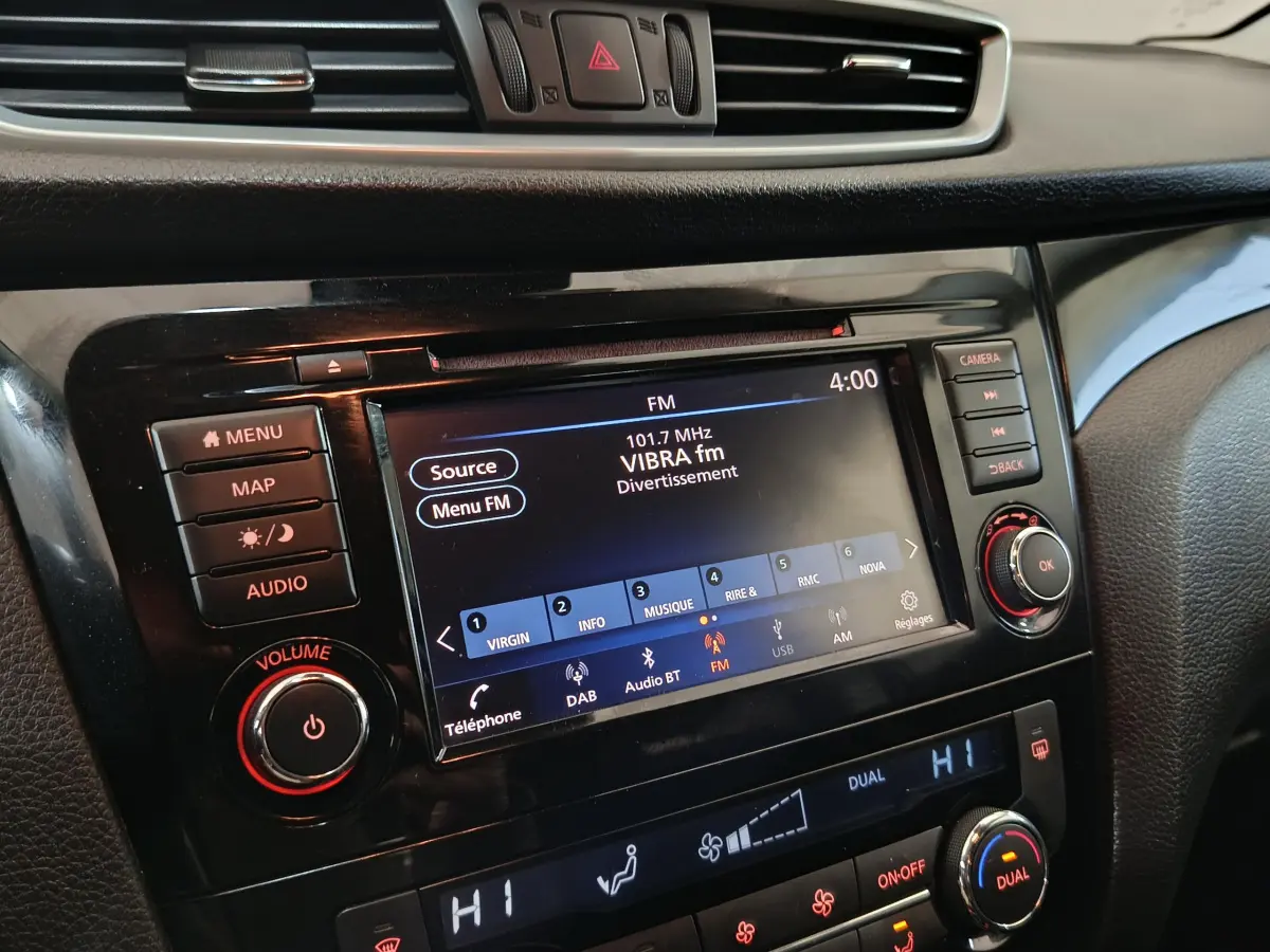 Gros plan sur l’écran tactile et la console centrale noire du Nissan Qashqai gris clair, affichant la radio FM et la climatisation.