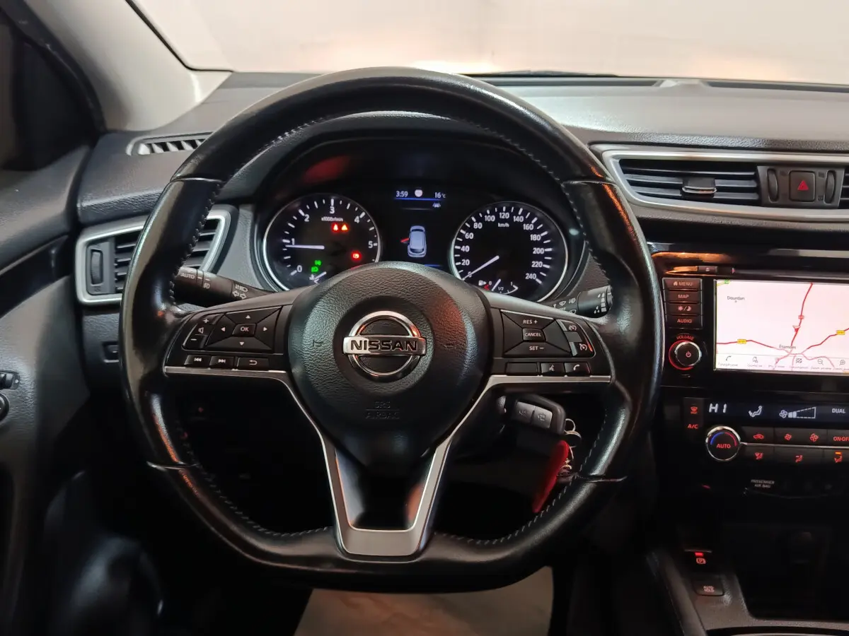 Vue intérieure centrée sur le volant cuir du Nissan Qashqai 2019 avec tableau de bord et écran tactile de navigation allumé.