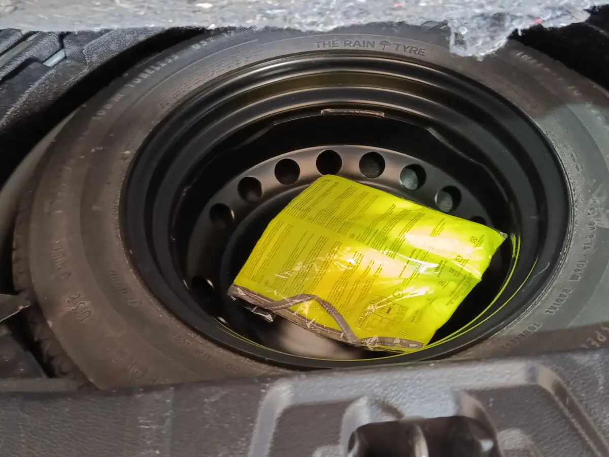 Gros plan sur la roue de secours galette noire avec un emballage jaune visible dans le coffre du Nissan Qashqai gris clair.