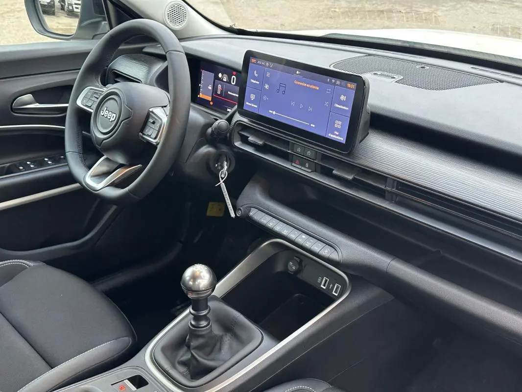 Vue intérieure côté conducteur du Jeep Avenger 2024, tableau de bord noir avec écran tactile et levier de vitesse manuel.