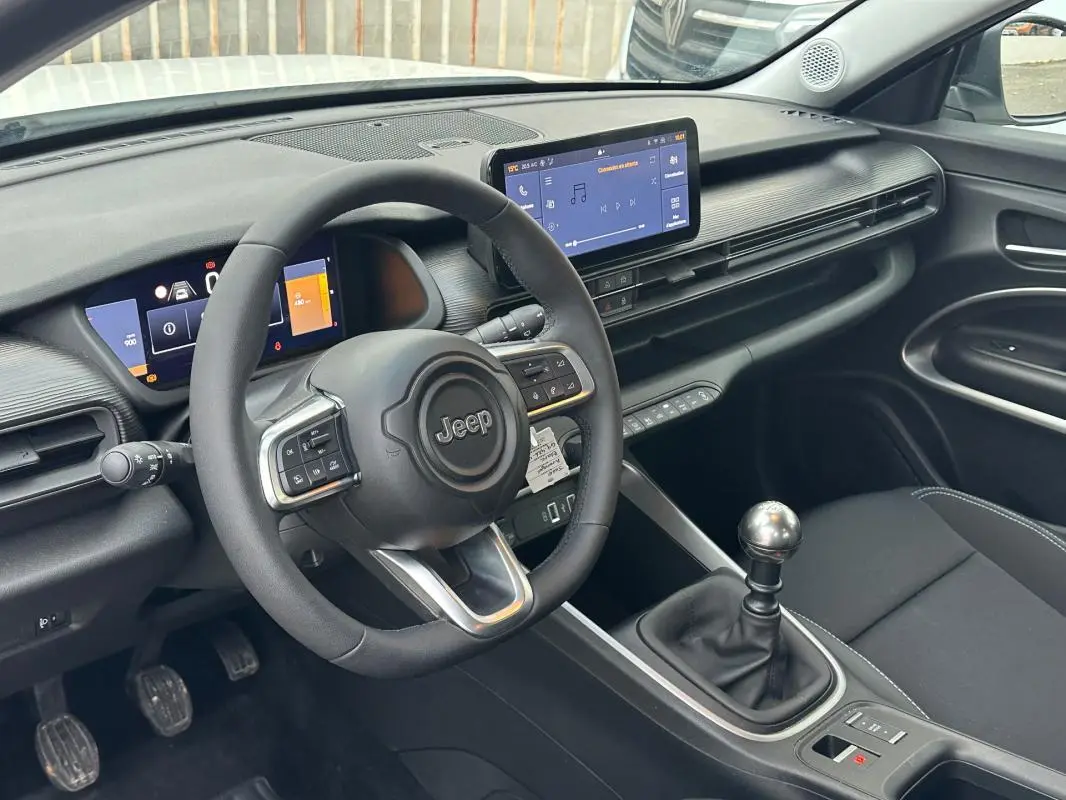 Vue intérieure côté conducteur du Jeep Avenger 2024, montrant le volant, tableau de bord numérique et levier de vitesse manuel.