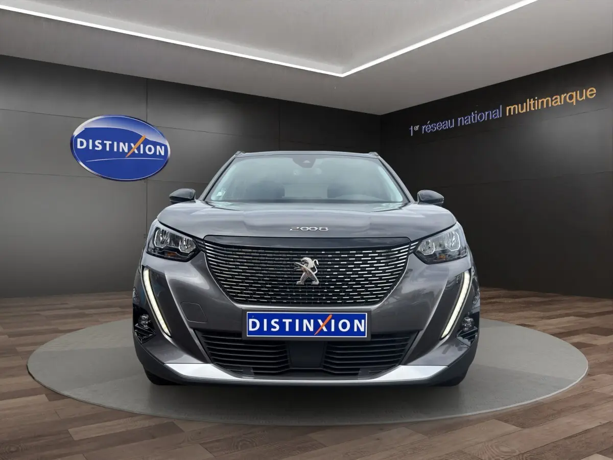 Peugeot 2008 gris foncé vue de face, avec calandre noire et feux LED verticaux allumés en showroom.