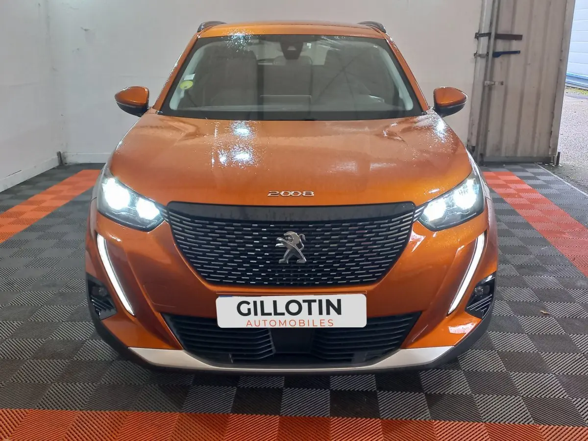Peugeot 2008 orange vue de face, phares LED allumés et calandre noire avec logo lion visible.