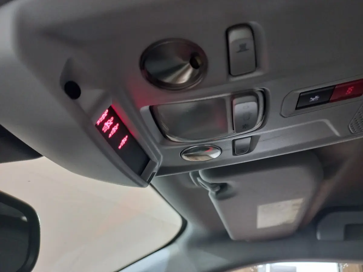 Vue intérieure du plafond avant de la Peugeot 2008 orange, montrant les commandes d'éclairage et le panneau SOS lumineux rouge.