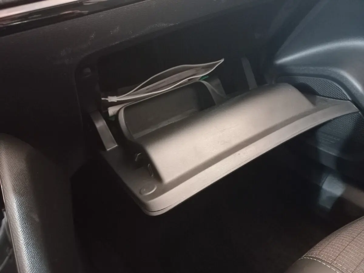 Gros plan sur la boîte à gants ouverte noire du Peugeot 2008 orange, avec des papiers et câbles visibles à l'intérieur.