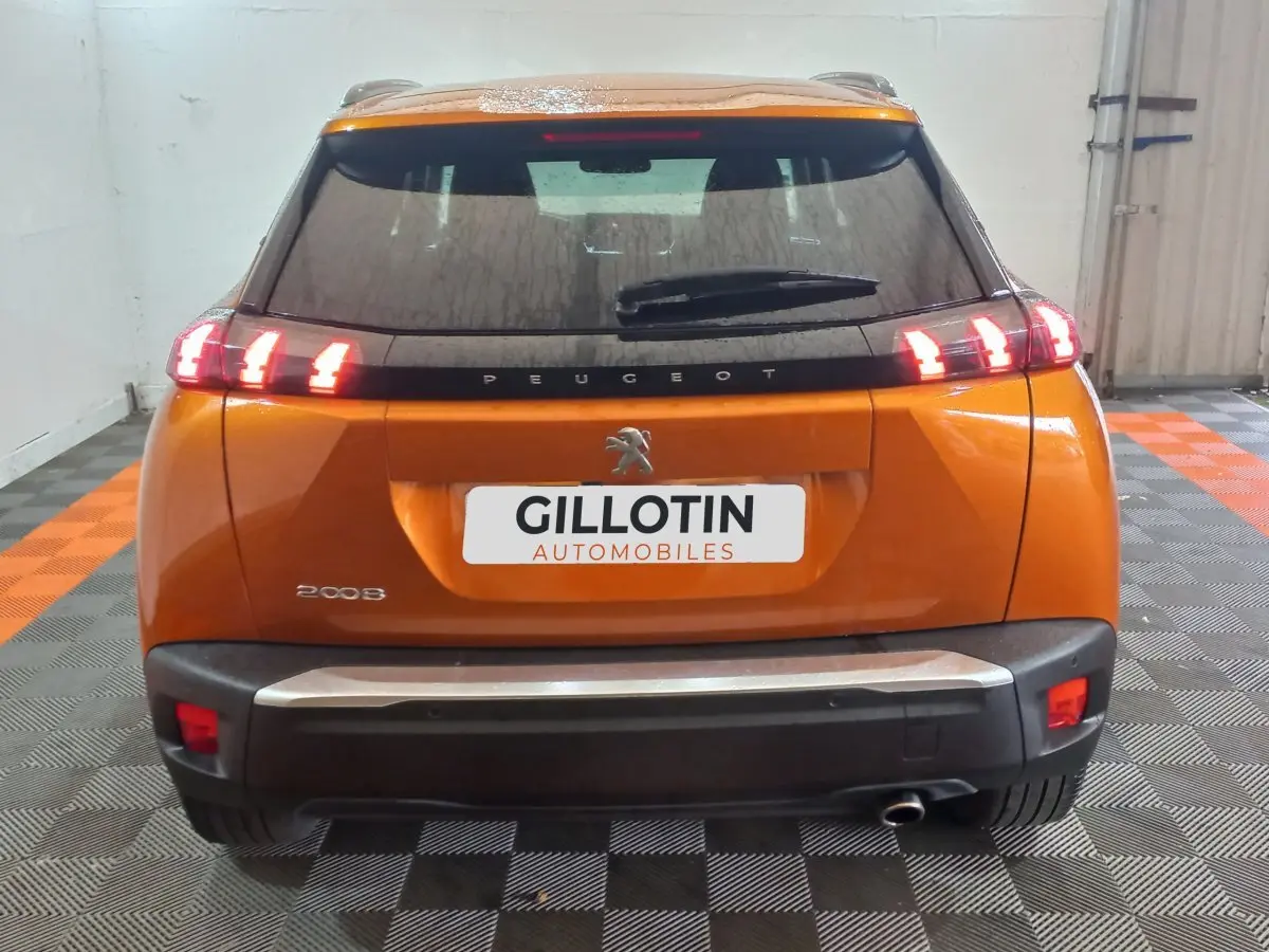 Vue arrière d'un Peugeot 2008 orange avec feux arrière allumés et logo lion visible sur le hayon.