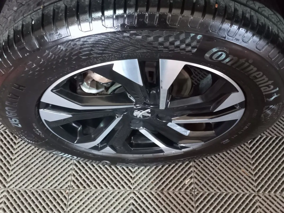Gros plan sur la jante alliage noire et argentée avec logo Peugeot, montée d'un pneu Continental.
