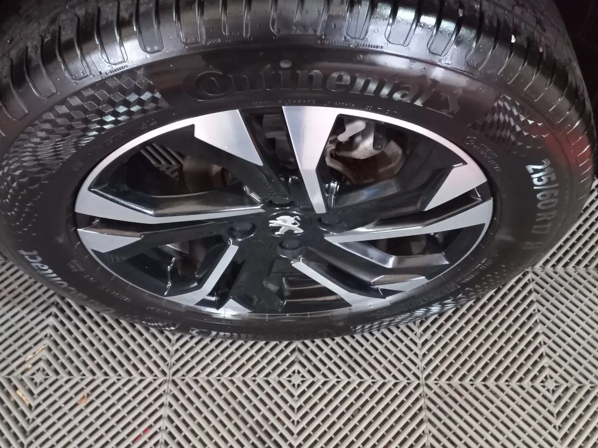 Gros plan sur la jante alliage noire et argentée avec logo Peugeot, montée d'un pneu Continental sur Peugeot 2008 orange.