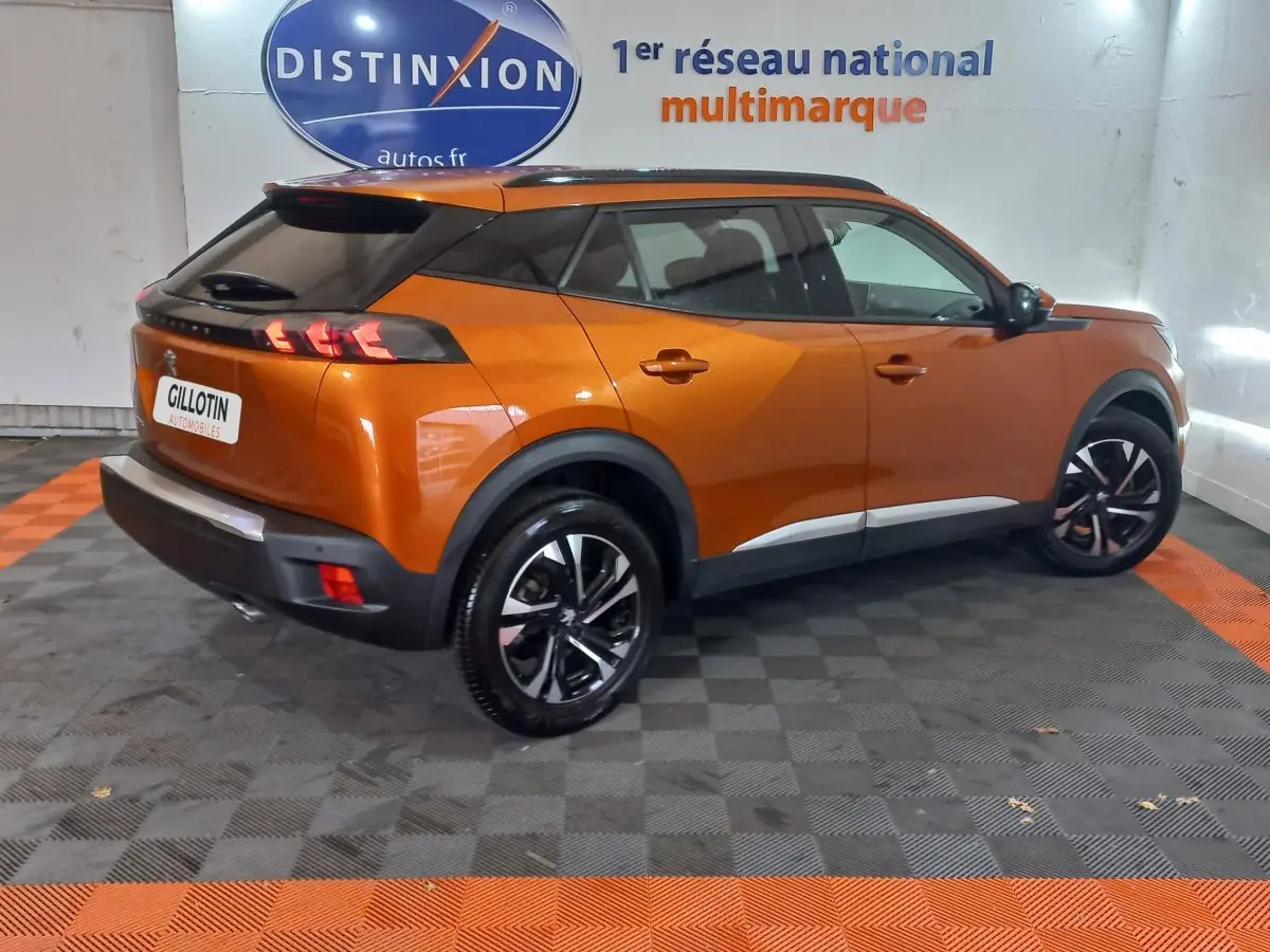 Peugeot 2008 orange vue 3/4 arrière droit en intérieur, avec jantes noires et toit noir contrasté.
