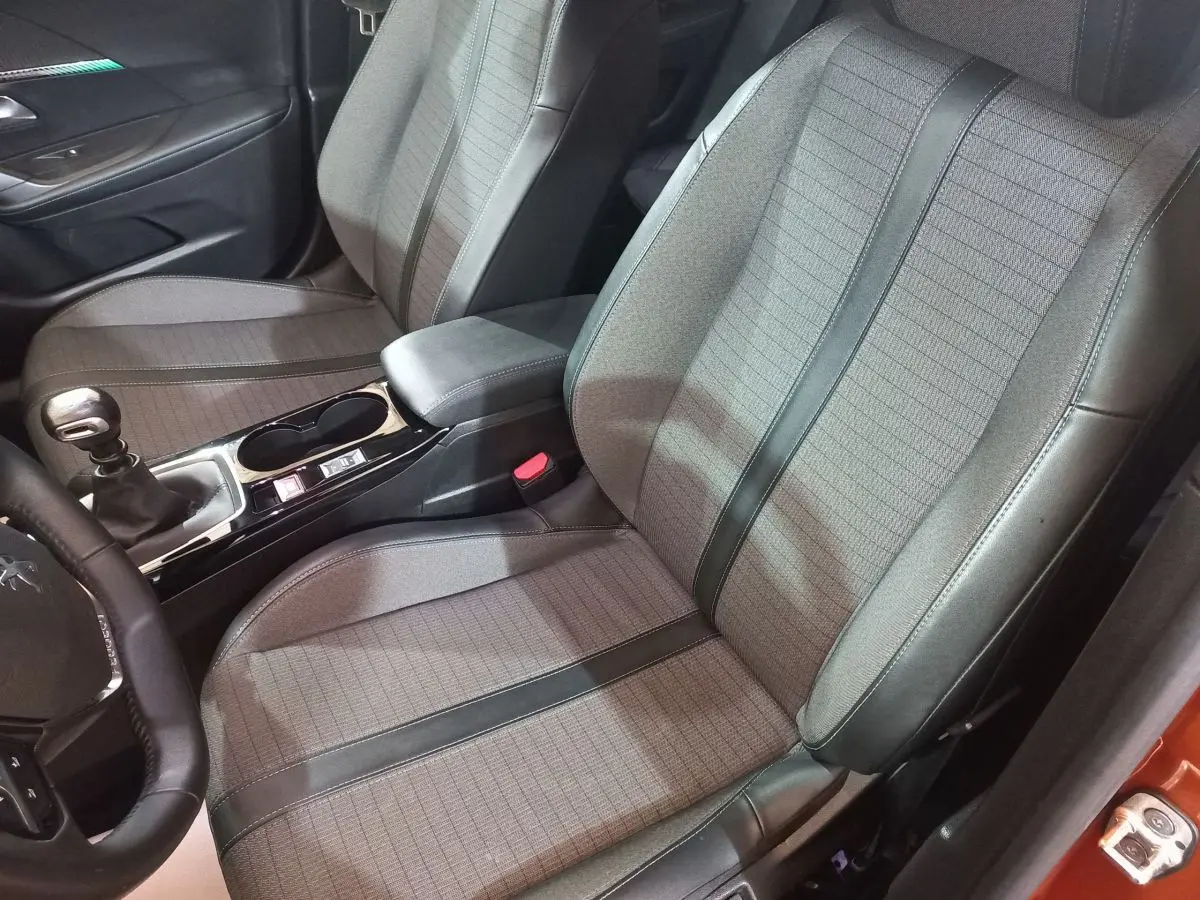 Vue intérieure côté conducteur du Peugeot 2008 orange 2021, montrant sièges tissu et cuir avec console centrale et levier de vitesse manuel.