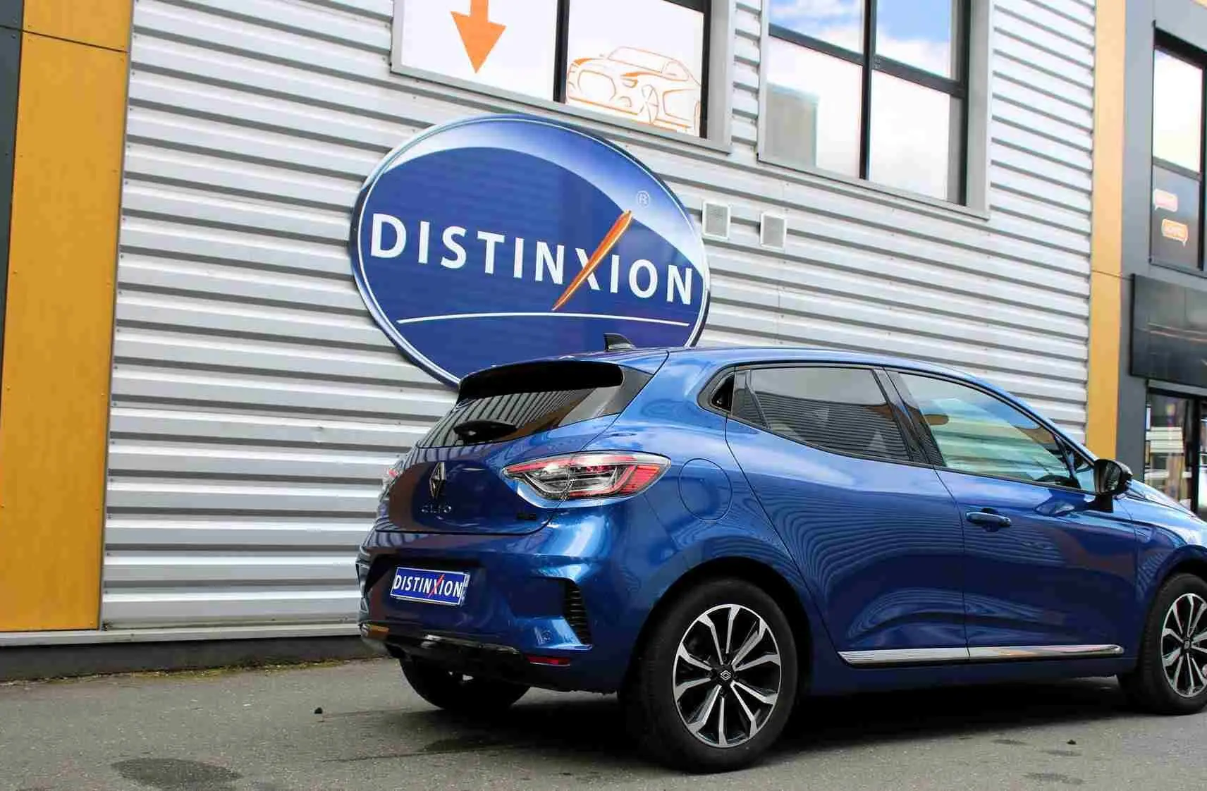 Vue 3/4 arrière droite d'une Renault Clio 2025 bleu Iron Metal avec jantes alliage et vitres teintées, stationnée devant un bâtiment.