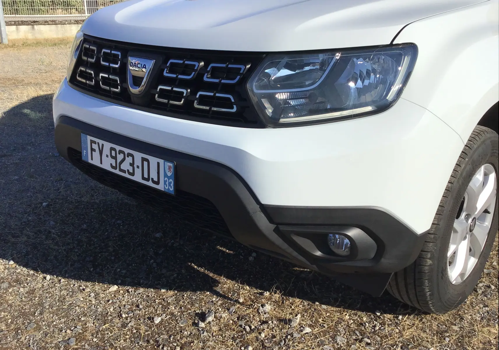 Gros plan sur l’avant droit du Dacia Duster blanc 2021, mettant en valeur la calandre noire et les phares LED.