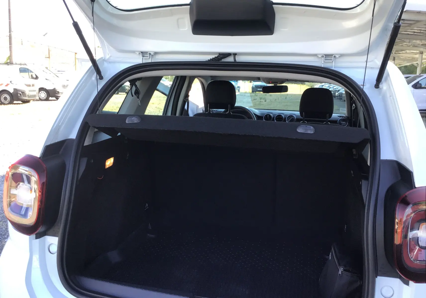 Vue arrière du coffre ouvert d'un Dacia Duster blanc 2021, montrant l'espace de chargement et l'intérieur sombre.