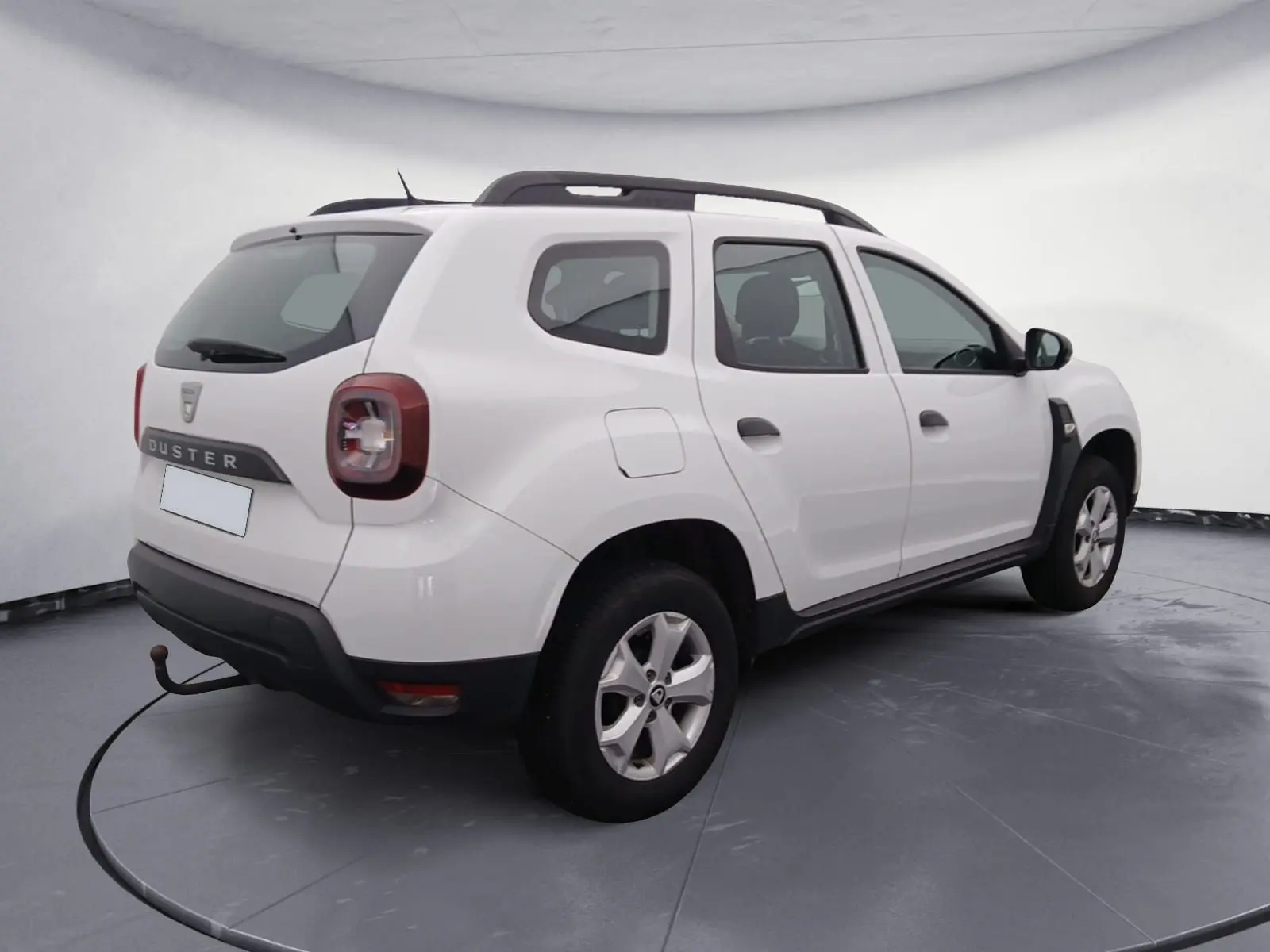 Vue 3/4 arrière droite d'un Dacia Duster blanc 2021 avec barres de toit noires et feux arrière LED.