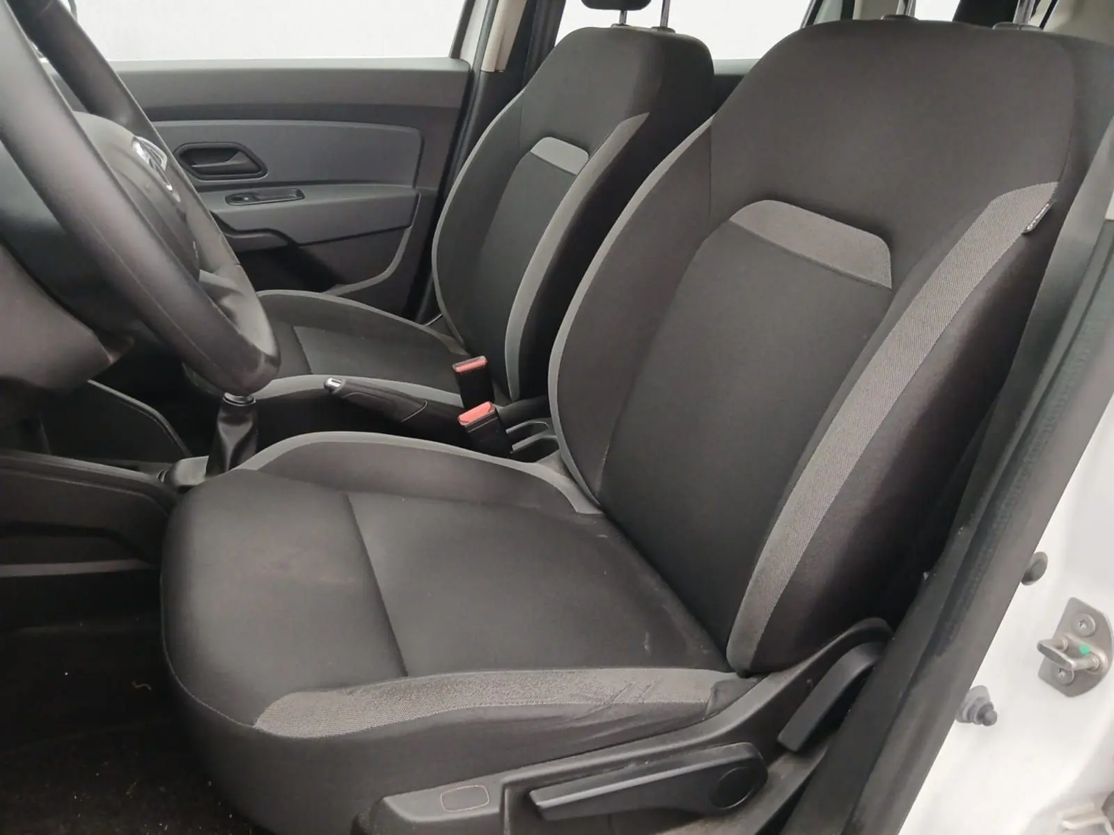Vue intérieure côté conducteur du Dacia Duster blanc 2021, sièges tissu noir avec détails gris et volant visible.
