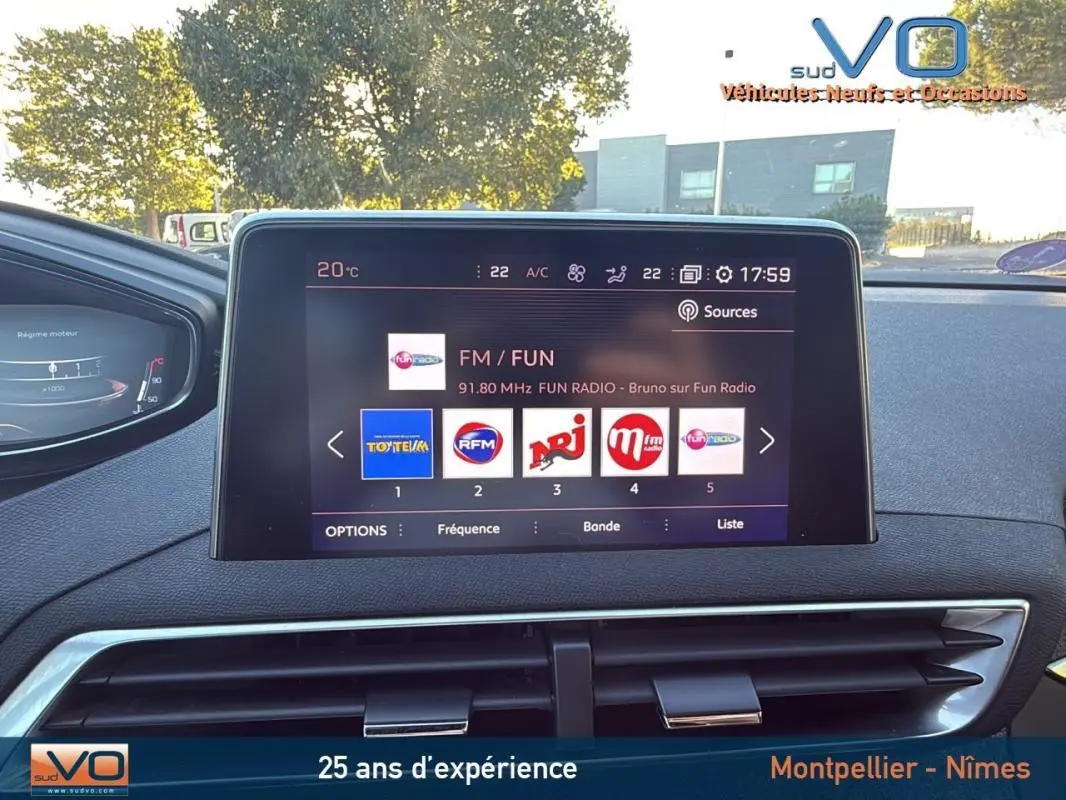 Vue intérieure centrée sur l'écran tactile du Peugeot 3008 gris foncé, affichant les stations radio FM avec tableau de bord en arrière-plan.