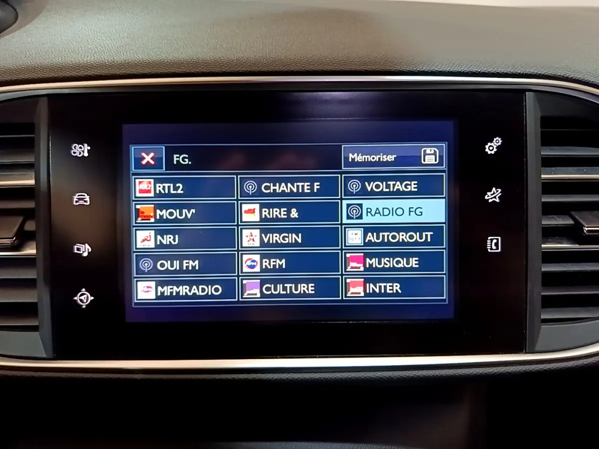Écran tactile central affichant les stations radio dans l’habitacle d’une Peugeot 308 gris foncé, vue de face.